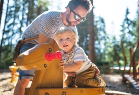 Papa peelt met peuter in speeltuin op speeltuig in bos